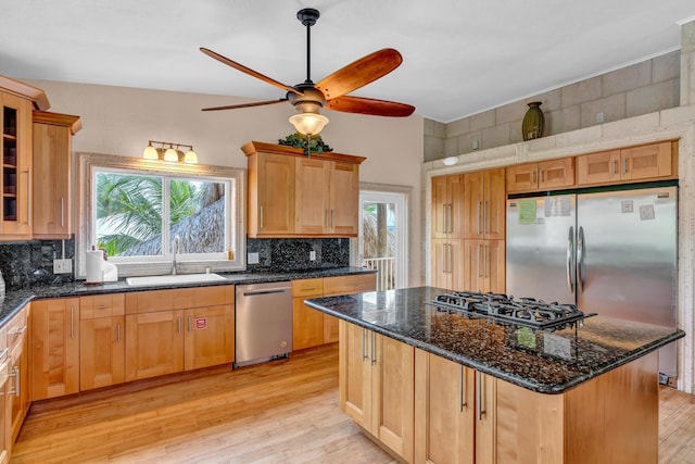 kitchen with sink, dark stone countertops, appliances with stainless steel finishes, a kitchen island, and backsplash