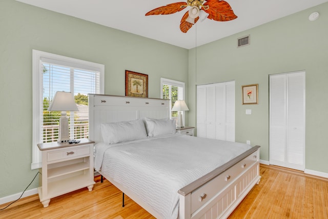 bedroom featuring multiple windows, ceiling fan, light hardwood / wood-style floors, and multiple closets