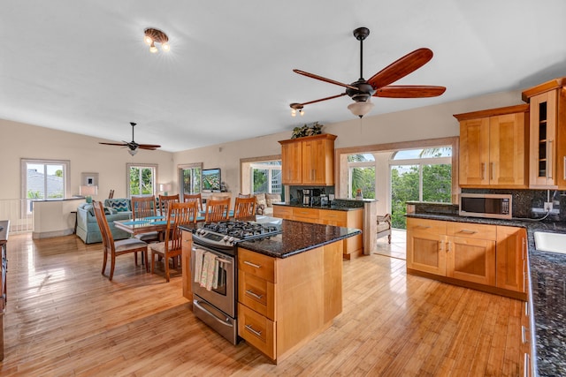 kitchen with tasteful backsplash, dark stone counters, a center island, stainless steel appliances, and light hardwood / wood-style flooring