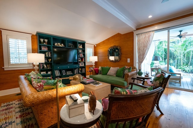 living area with ceiling fan, vaulted ceiling, wooden walls, and wood finished floors