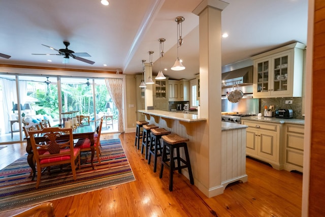 kitchen with a kitchen breakfast bar, light wood finished floors, tasteful backsplash, glass insert cabinets, and pendant lighting