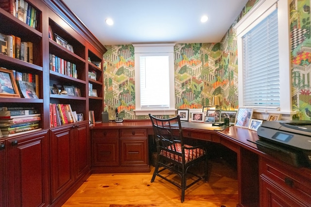 home office with built in study area, light wood-style flooring, and wallpapered walls