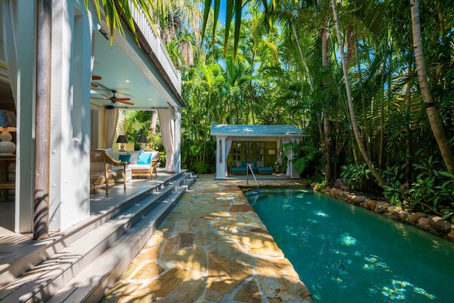 outdoor pool with a patio area, ceiling fan, and an outbuilding