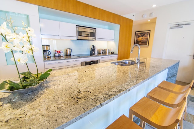 kitchen with sink, appliances with stainless steel finishes, white cabinetry, a kitchen breakfast bar, and light stone countertops