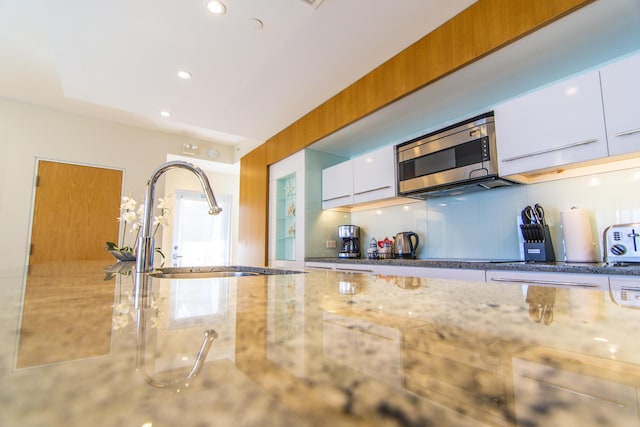 kitchen with backsplash, light stone countertops, sink, and white cabinets