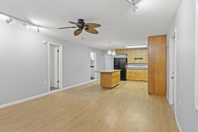 kitchen featuring ceiling fan, a center island, decorative light fixtures, black refrigerator with ice dispenser, and light wood-type flooring