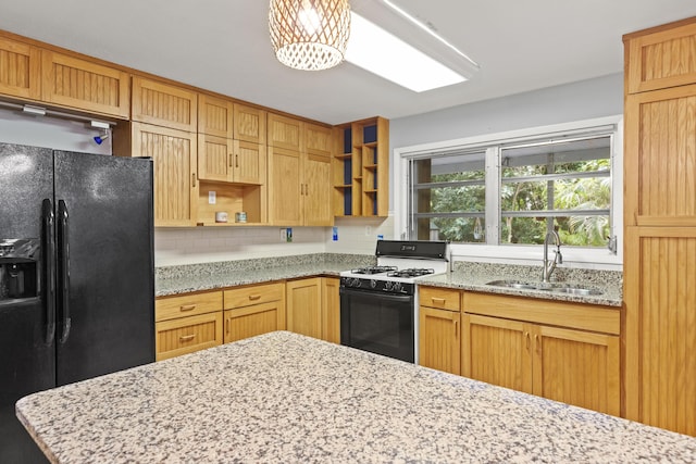 kitchen with sink, decorative backsplash, black fridge, gas range, and light stone countertops