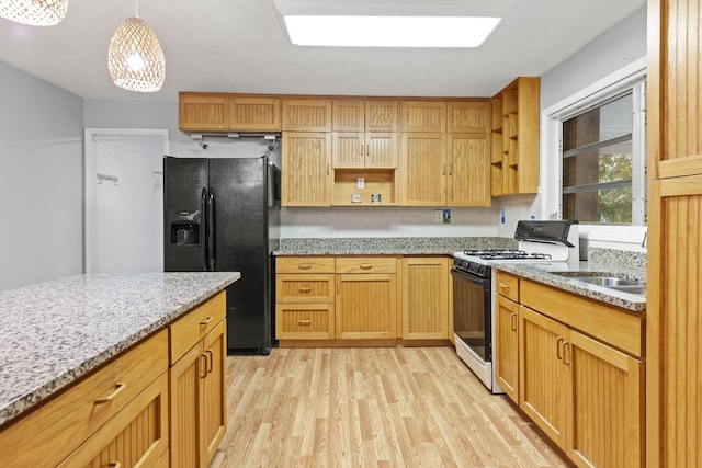 kitchen featuring light hardwood / wood-style floors, light stone countertops, gas stove, black fridge, and decorative light fixtures