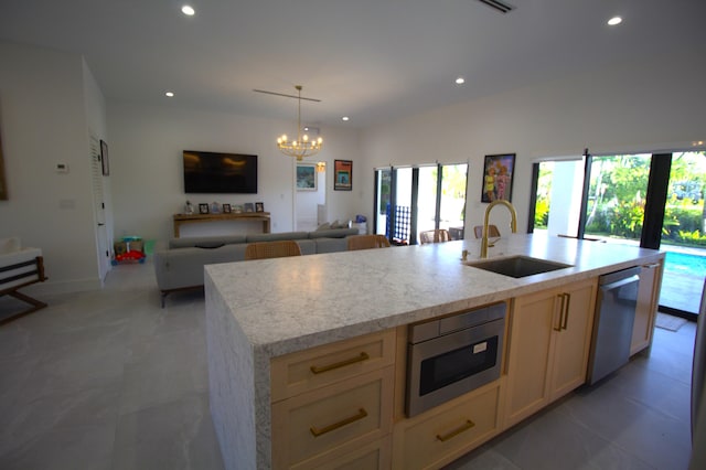 kitchen featuring a kitchen island with sink, sink, light stone countertops, and appliances with stainless steel finishes