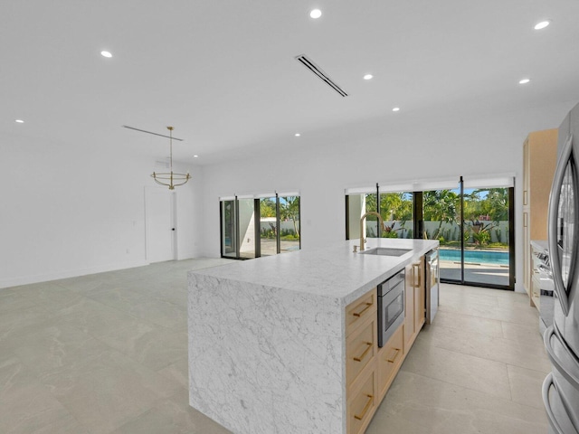 kitchen featuring light brown cabinetry, decorative light fixtures, sink, stainless steel appliances, and a center island with sink