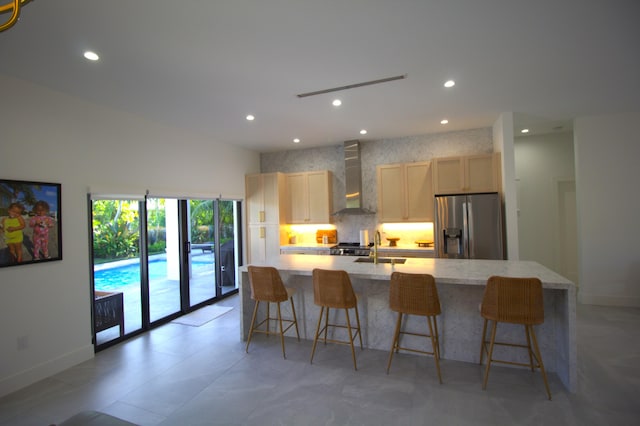 kitchen with stainless steel refrigerator with ice dispenser, a breakfast bar, sink, a large island with sink, and wall chimney range hood