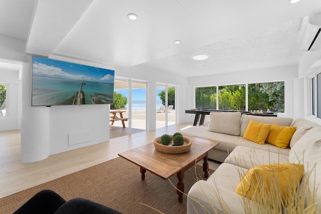 living room featuring an AC wall unit, a wealth of natural light, a textured ceiling, and light hardwood / wood-style floors