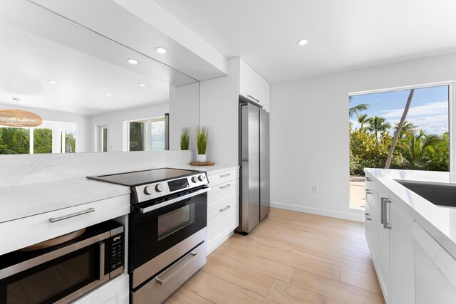 kitchen featuring appliances with stainless steel finishes, white cabinetry, sink, light stone counters, and light hardwood / wood-style floors