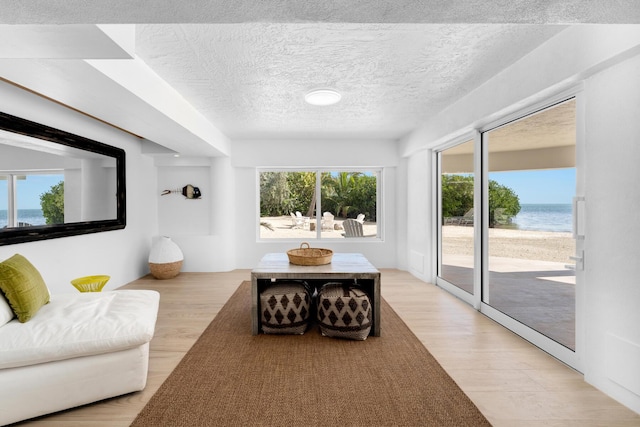 living room featuring light wood-type flooring, a textured ceiling, and a water view