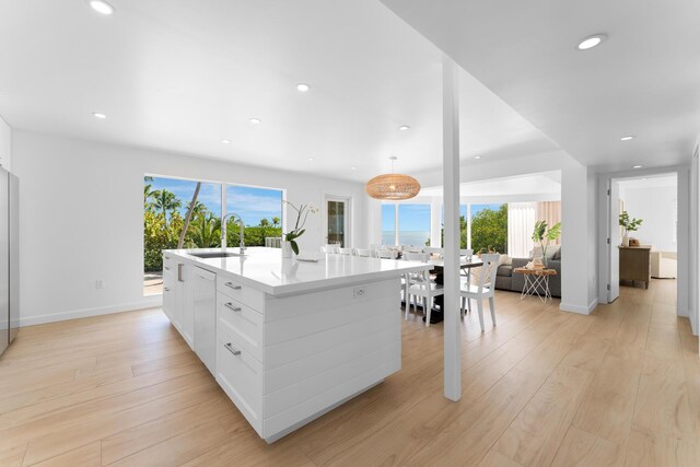 kitchen featuring an island with sink, light hardwood / wood-style flooring, white cabinets, and decorative light fixtures