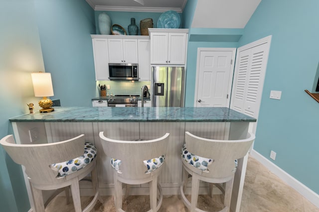 kitchen with tasteful backsplash, white cabinets, a kitchen breakfast bar, stainless steel appliances, and stone counters