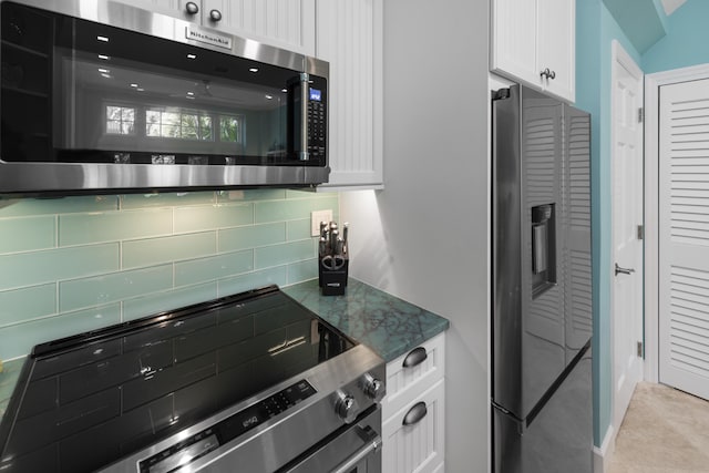 kitchen featuring white cabinets, appliances with stainless steel finishes, decorative backsplash, and dark stone counters