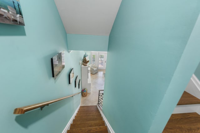 stairway featuring lofted ceiling, wood finished floors, and baseboards