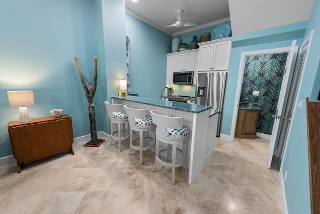 kitchen with appliances with stainless steel finishes, a kitchen breakfast bar, ornamental molding, a peninsula, and white cabinetry