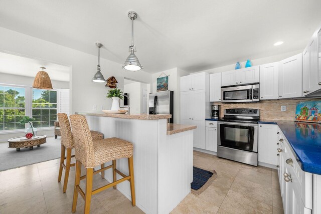 kitchen with appliances with stainless steel finishes, pendant lighting, white cabinetry, a breakfast bar area, and backsplash