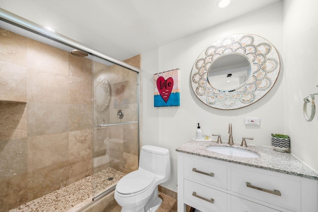 bathroom featuring a shower with door, vanity, and toilet