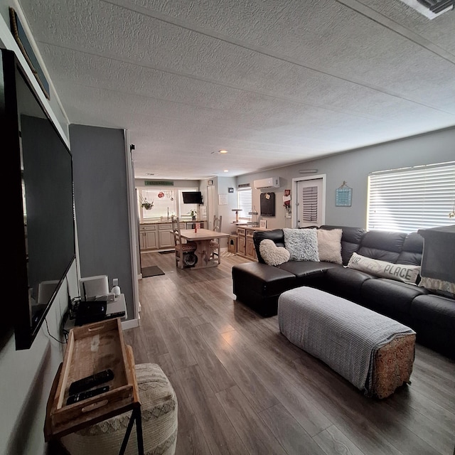 living room with hardwood / wood-style floors, a wealth of natural light, a wall mounted AC, and a textured ceiling