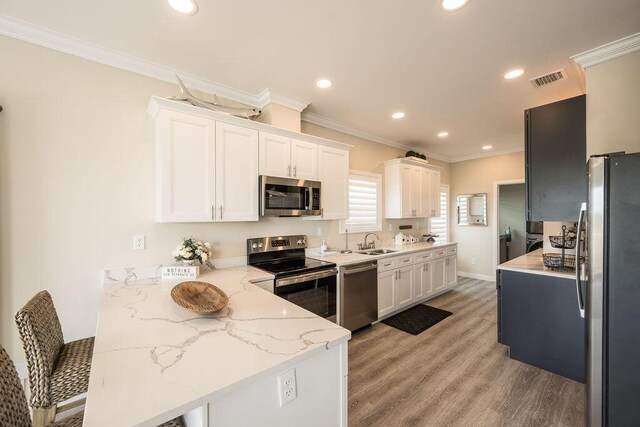 kitchen with appliances with stainless steel finishes, white cabinetry, sink, light stone countertops, and light wood-type flooring