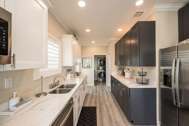 kitchen with sink, appliances with stainless steel finishes, white cabinetry, light stone counters, and stacked washer / drying machine