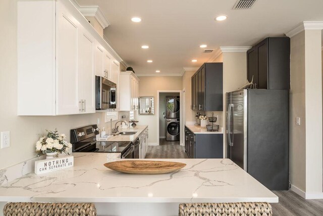 kitchen featuring stacked washer / dryer, sink, kitchen peninsula, stainless steel appliances, and light stone countertops