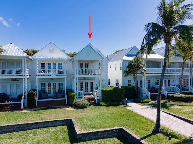 back of property featuring french doors, a balcony, and a lawn