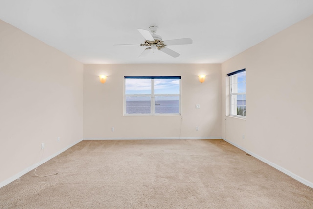 spare room with a ceiling fan, baseboards, and light carpet