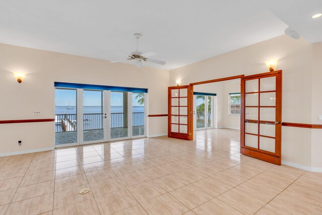 tiled empty room with french doors, ceiling fan, and a water view