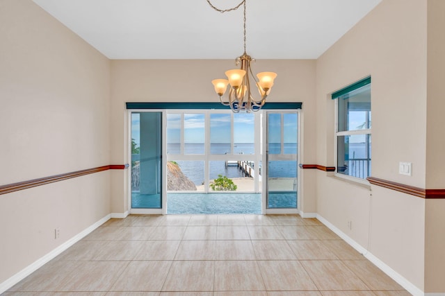 unfurnished dining area featuring tile patterned flooring, an inviting chandelier, baseboards, and a water view