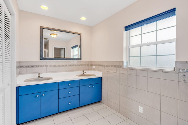 full bath featuring double vanity, tile patterned floors, tile walls, and a sink