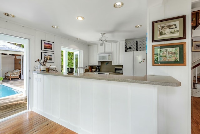 kitchen featuring a peninsula, white appliances, a toaster, and white cabinetry