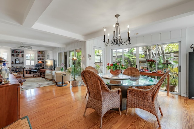 dining area featuring light wood finished floors, built in shelves, beam ceiling, and ceiling fan with notable chandelier