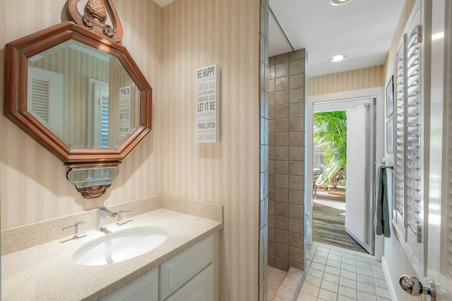 bathroom with wallpapered walls, vanity, a tile shower, and tile patterned floors