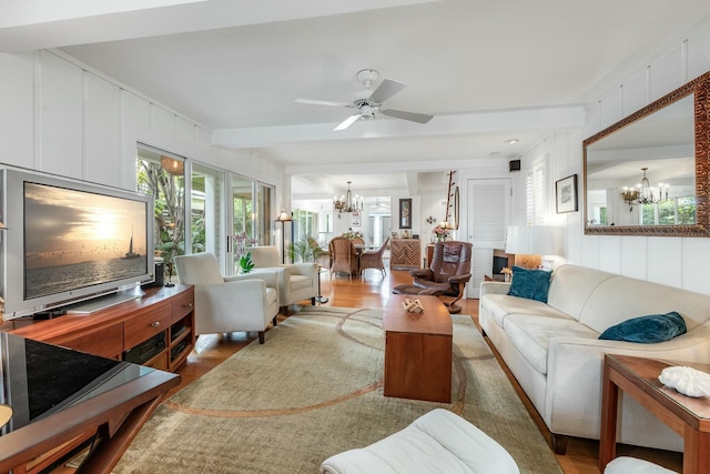 living room with ceiling fan with notable chandelier, beamed ceiling, wood finished floors, and a decorative wall