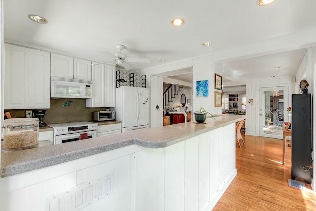 kitchen with white appliances, a toaster, light wood-style flooring, a peninsula, and light countertops