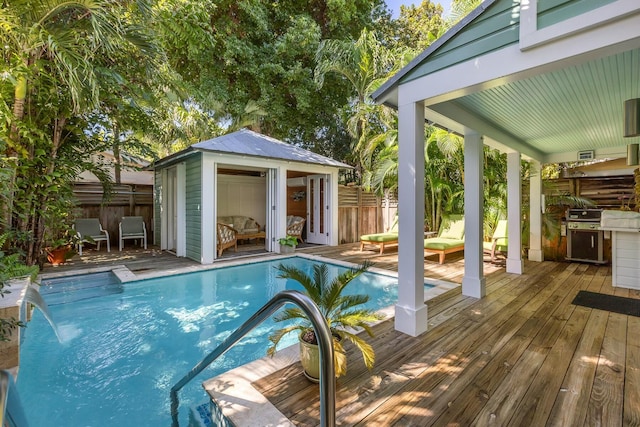 view of pool with an outdoor structure, fence, grilling area, a wooden deck, and a fenced in pool