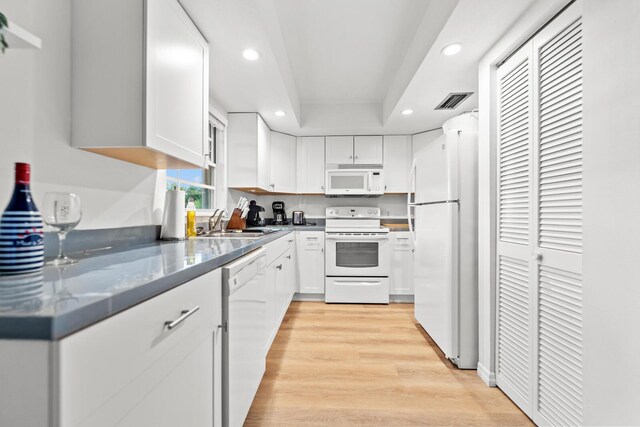 kitchen featuring sink, white appliances, a tray ceiling, white cabinets, and light wood-type flooring