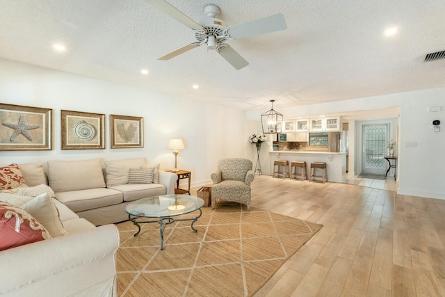 living area with light wood-style flooring, recessed lighting, ceiling fan with notable chandelier, and a textured ceiling