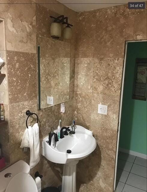 bathroom with toilet, tile patterned flooring, and tile walls