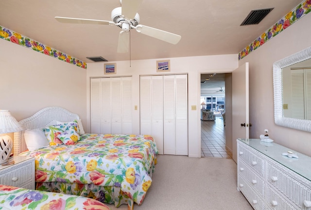 bedroom featuring ceiling fan, light colored carpet, and multiple closets