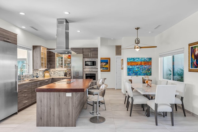 kitchen with wood counters, sink, tasteful backsplash, built in appliances, and island exhaust hood