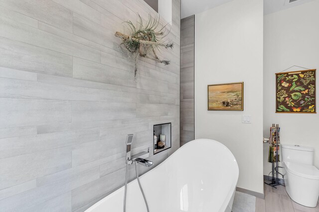 bathroom with a tub to relax in and toilet