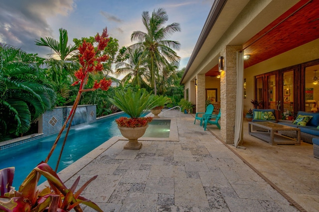 pool at dusk featuring pool water feature and a patio