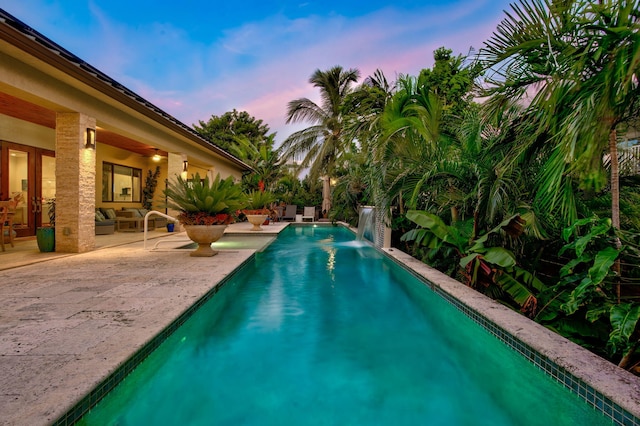 pool at dusk with a patio and pool water feature