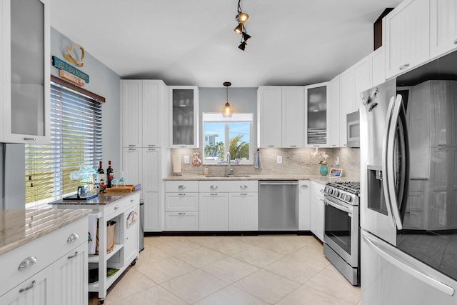 kitchen featuring sink, white cabinetry, light stone counters, appliances with stainless steel finishes, and pendant lighting