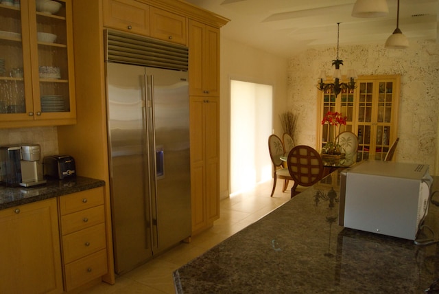 kitchen with built in fridge, pendant lighting, dark stone counters, and light tile patterned floors